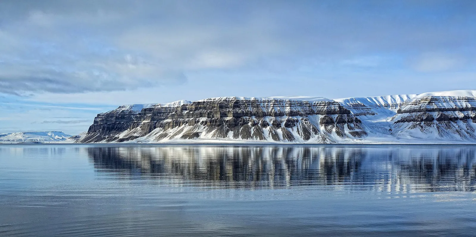 The snow-covered, cliff-banded mountain Templet reflected in the still water of Tempelfjorden on a clear April day