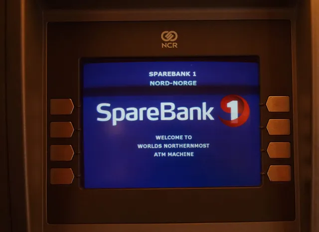 Der Bildschirm eines Geldautomaten in dunklem Rahmen mit dem Logo von SpareBank 1 und der Meldung „Welcome to world's northernmost ATM machine“